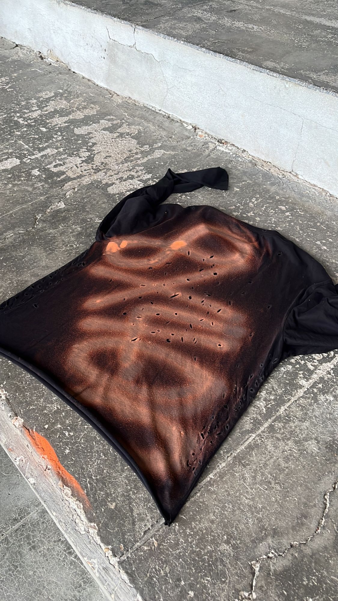 Camiseta 8x400 negra de manga larga sobre el asfalto, con el logo pintado en spray naranja en la espalda y agujeros hechos a mano